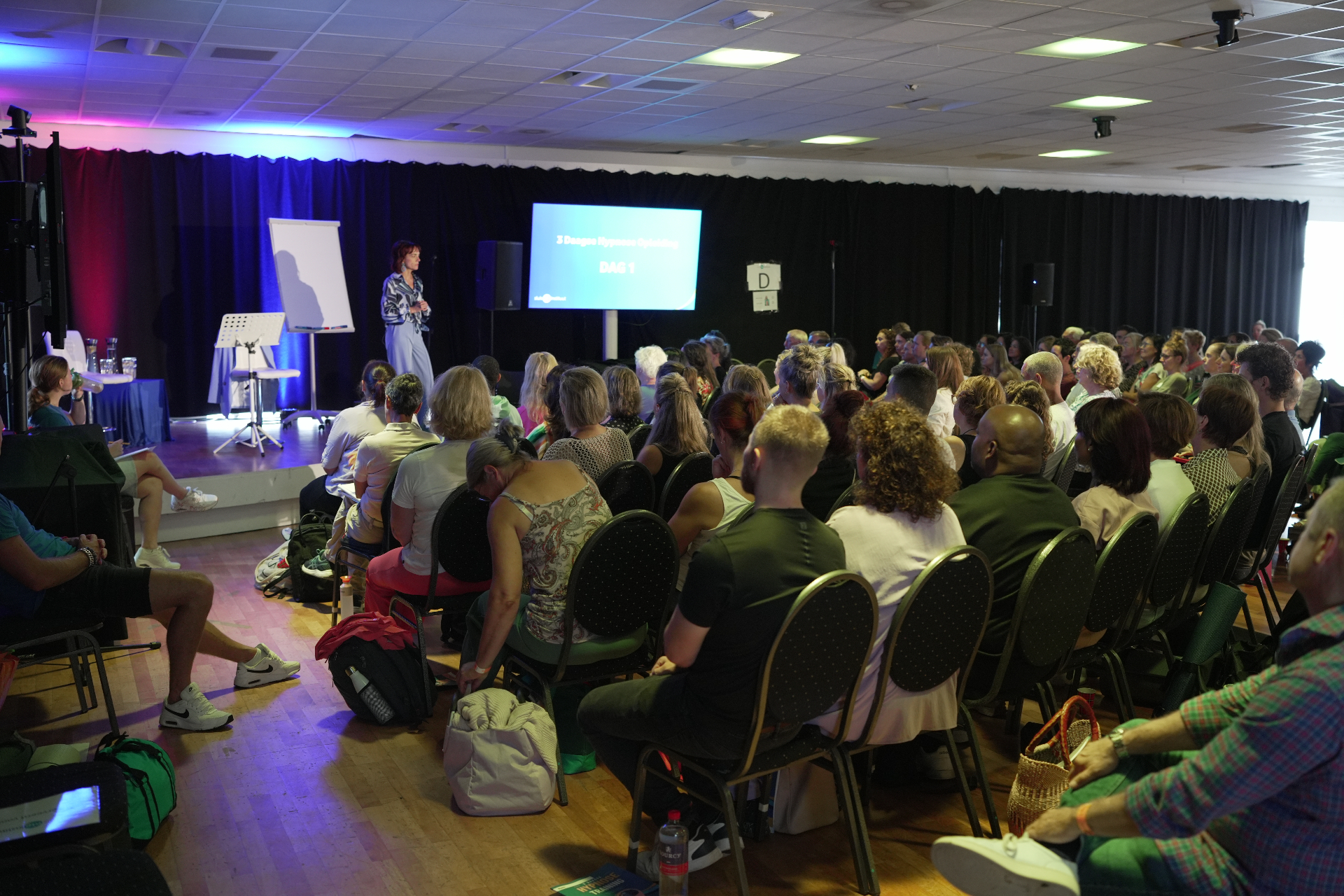 Volle zaal van 100 deelnemers tijdens een live hypnosedag